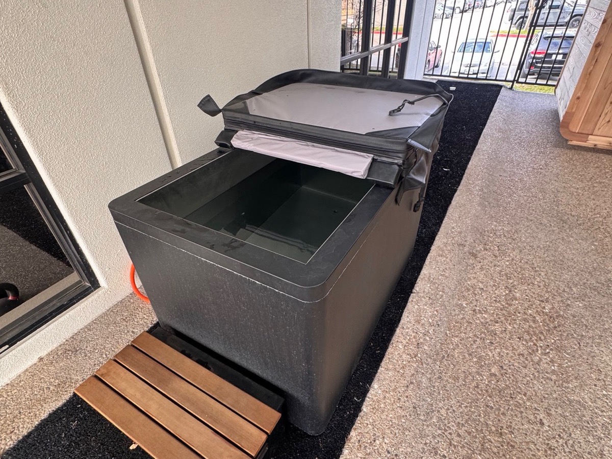 The cold plunge with its lid open and a wooden step beside it, on the covered patio at WLF Club.