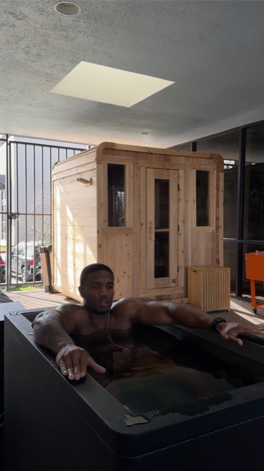 A member in the WLF cold plunge with the sauna behind him.